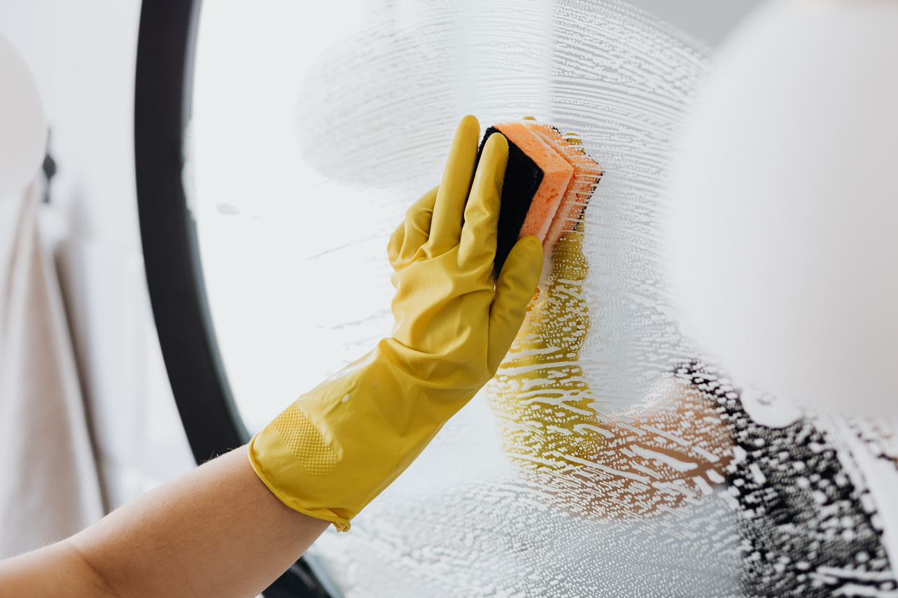 Faceless person cleaning mirror with sponge